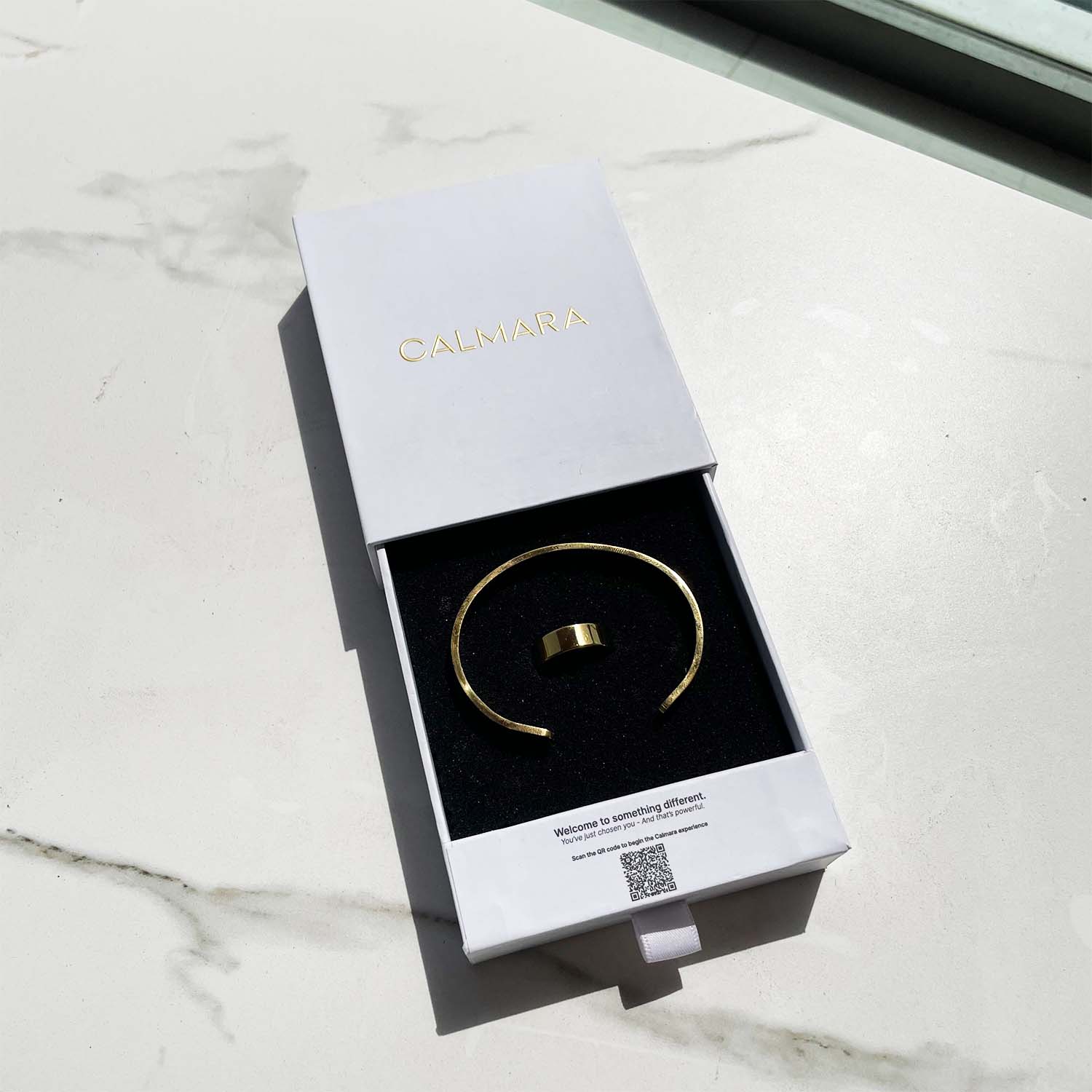 Gold bracelet in a white box with 'Calmara' branding on a marble surface