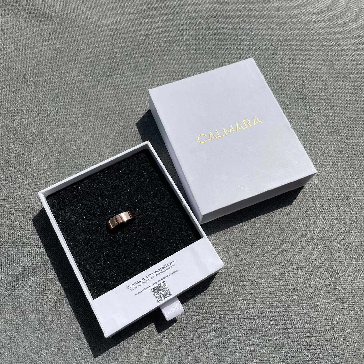 Gold ring in a Calmara branded box on a gray surface