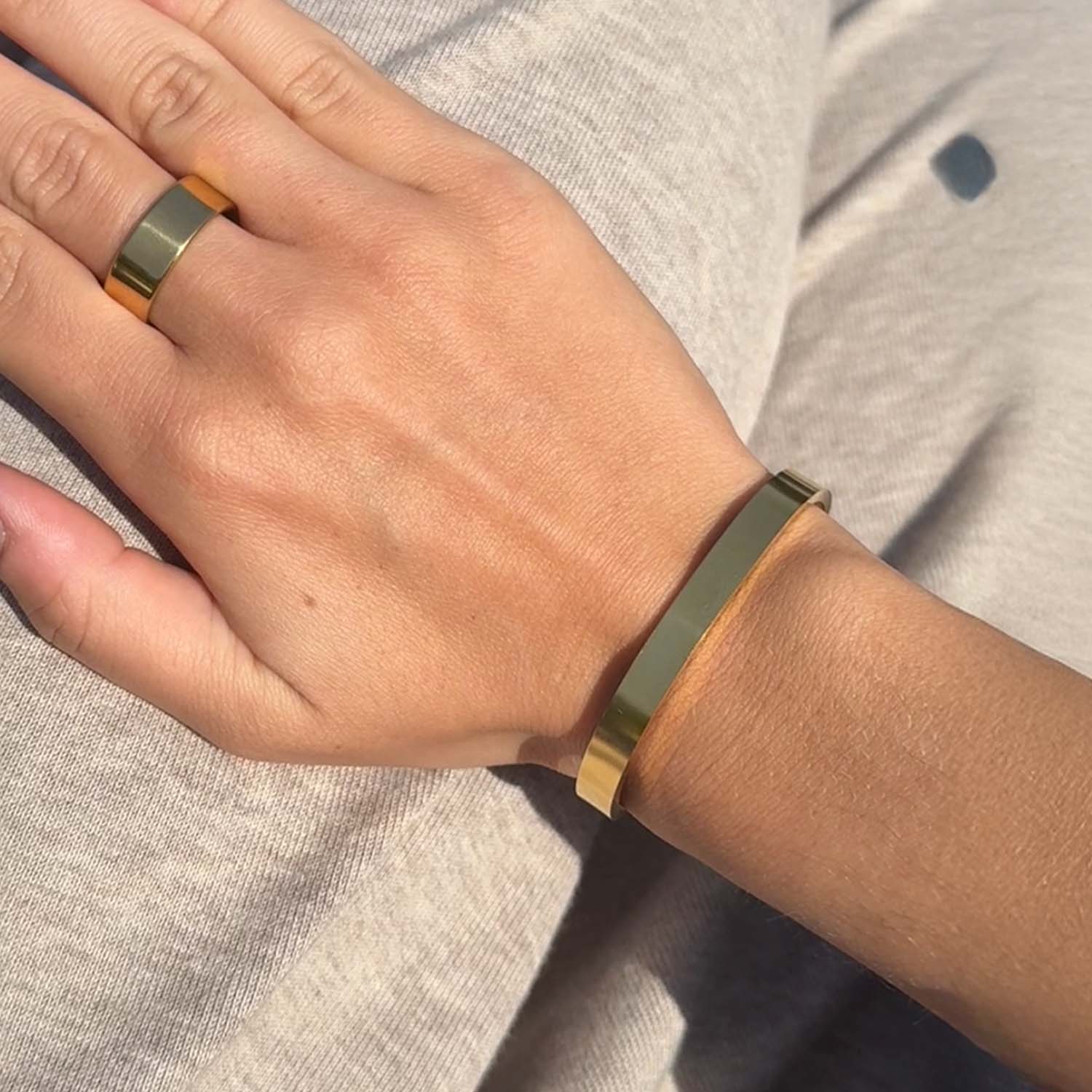 Hand wearing a gold ring and bracelet on a neutral background