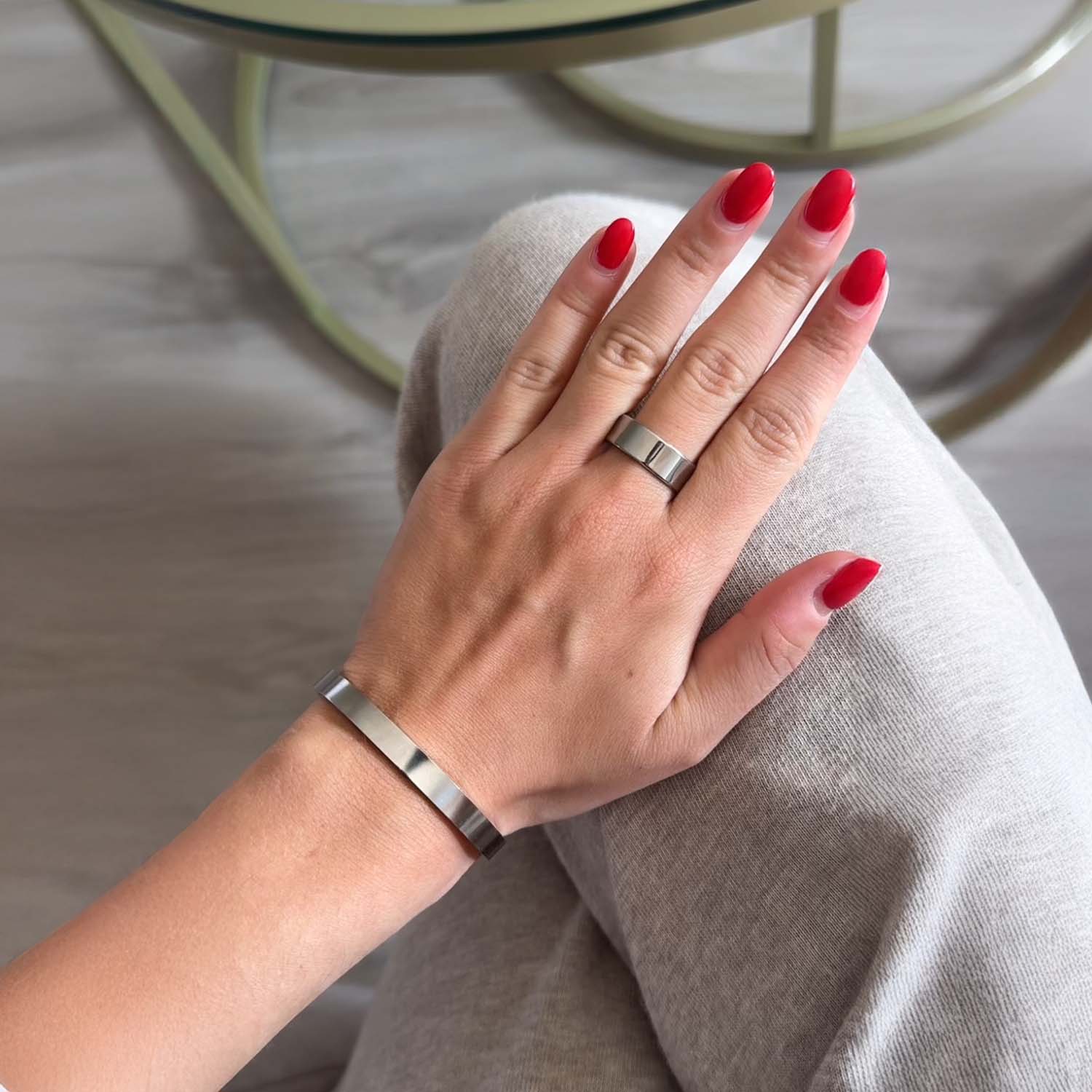 Hand with red nail polish wearing a silver ring and bracelet on a light surface.