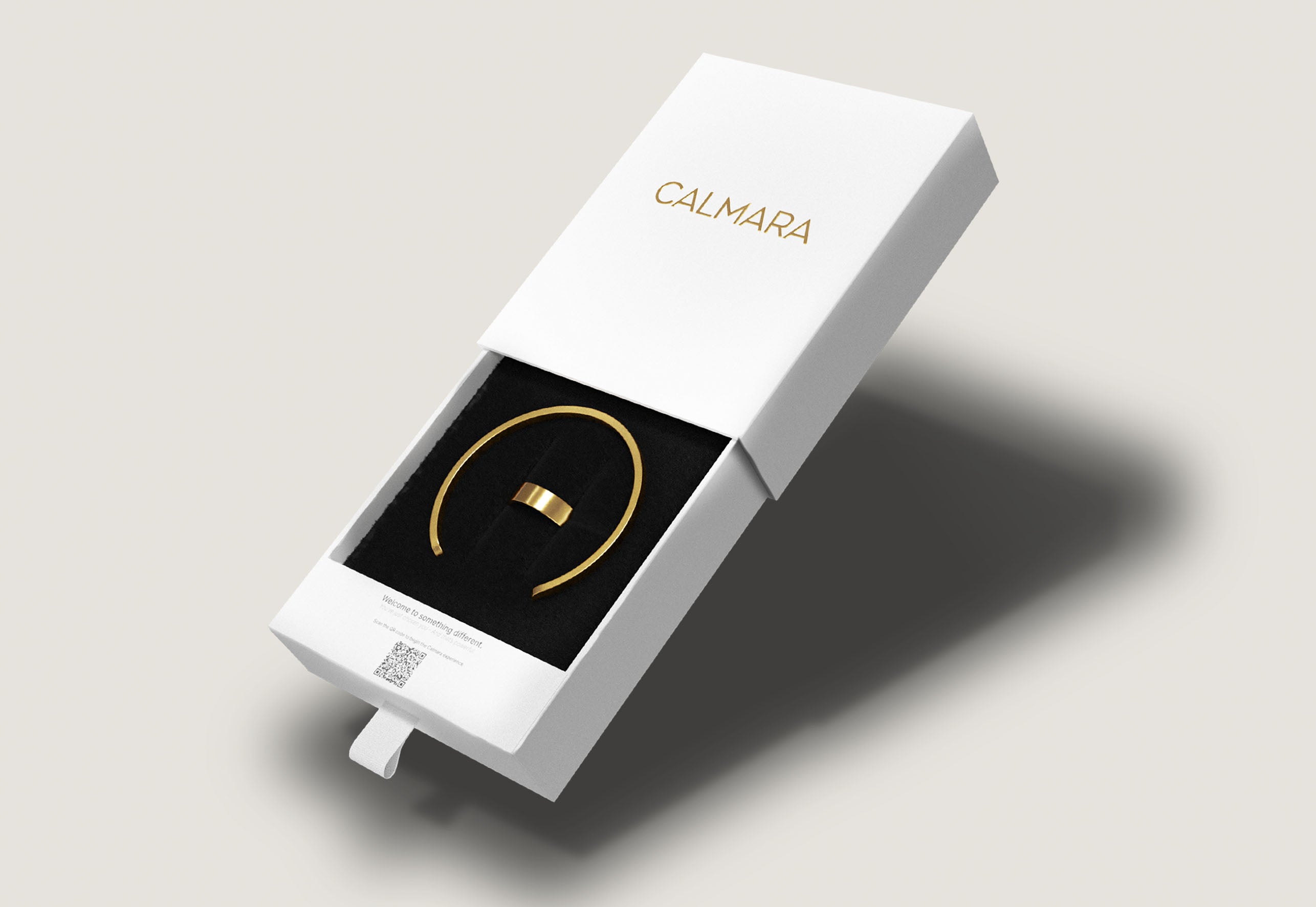 White jewelry box with a gold ring on a gray background, featuring the brand 'Calmara'.
