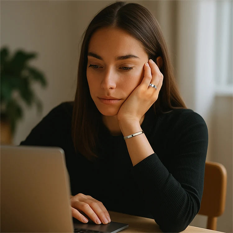 Woman sitting at a table with a laptop, looking thoughtful while using calmara set.